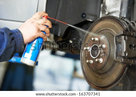 car mechanic cleaning car wheel brake disk from rust corrosion at automobile repair service station
