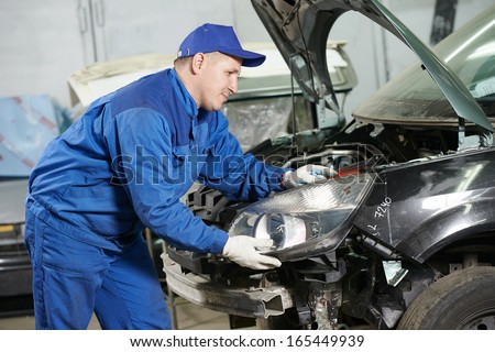 mechanic matching automobile headlight lamp to damaged car at repair service station mechanic matching automobile headlight lamp to damaged car at repair service station