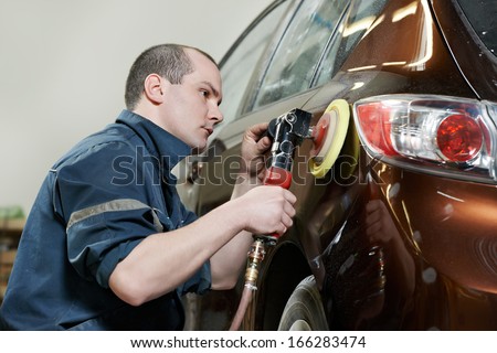 Auto Mechanic Worker Polishing Bumper Car At Automobile Repair And Renew Service Station Shop By Power Buffer Machine