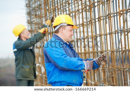 builder workers knitting metal rods bars into framework reinforcement for concrete pouring at construction site