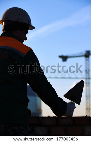 silhouette of construction mason worker bricklayer installing red brick with trowel putty knife outdoors