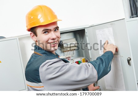 Happy young adult electrician builder engineer worker in front of fuse switch board