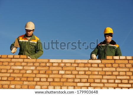 two construction mason worker bricklayer installing red brick with trowel putty knife outdoors