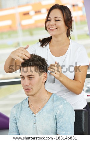 Female hairdresser cutting hair of smiling man client at beauty parlour
