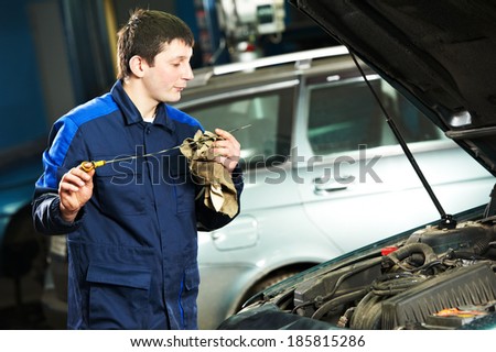 auto mechanic technician examining level during replacing and pouring motor oil into automobile engine at maintenance repair service station