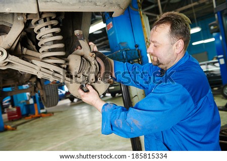 car mechanic inspecting car wheel and suspension detail of lifted automobile at repair service station