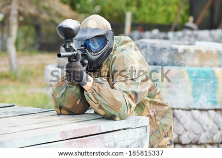 paintball sport player man in protective camouflage uniform and mask with marker gun outdoors