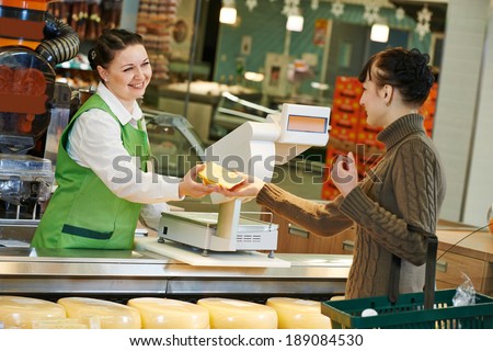 Sales assistant in supermarket demonstrating food cheese to female customer during shopping at store
