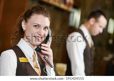 Happy female receptionist worker with phone standing at hotel counter