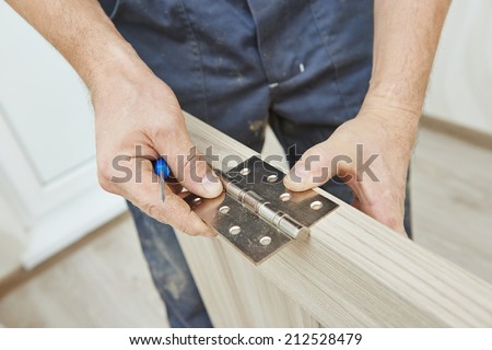 Close-up carpenter process of wood door hinge installation.