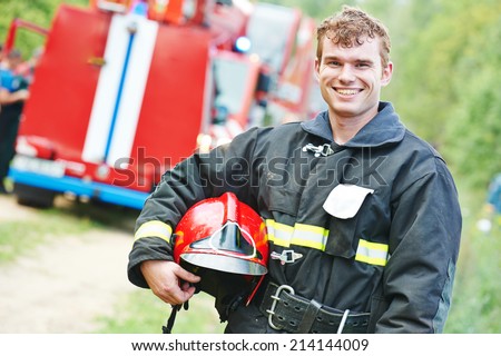 young smiling fireman firefighter in uniform in front of fire engine machine