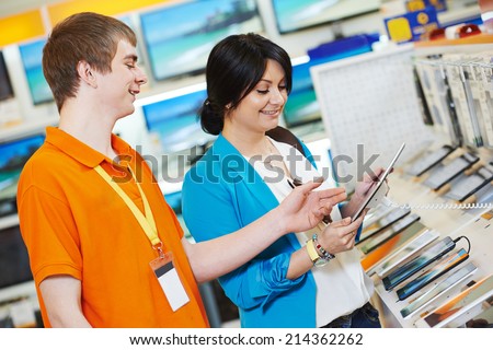 Young woman choosing tablet pc computer set with shop assistant in home appliance shopping mall supermarket