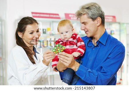 Cheerful female pharmacist chemist showing tablet vitamins to father man with little baby child girl in pharmacy drugstore