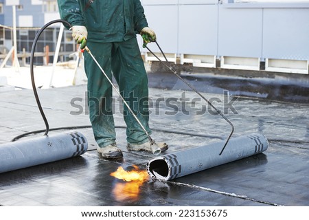 Roofer installing Roofing felt with heating and melting of bitumen roll by torch on flame during roof repair