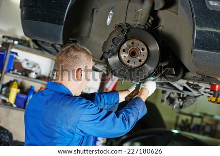 car mechanic worker repairing suspension of lifted automobile at auto repair garage shop station