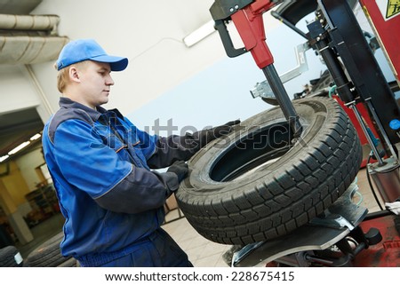Auto repairman loading automobile car wheel at tyre fitting machine during tire replacing