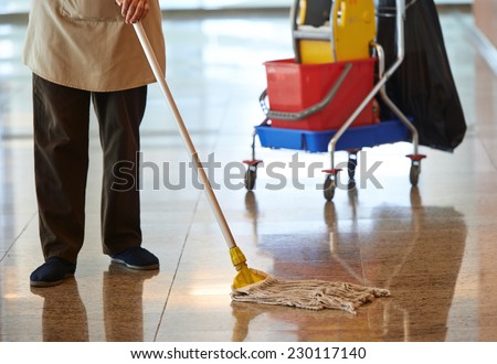 cleaner with mop and uniform cleaning hall floor of public business building