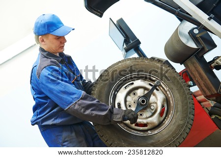 Auto repairman loading automobile car wheel at tyre fitting machine during tire replacing