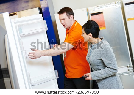 shop assistant demonstrates refrigerator to young woman in home appliance shopping mall supermarket