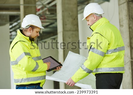 young male engeneers workers foreman at a indoors building site with blueprints