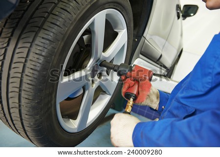 car mechanic screwing or unscrewing car wheel of lifted automobile at repair service station