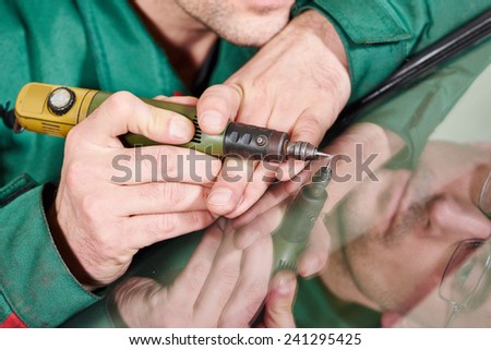 Automobile glazier repairman at windscreen repair of a car in auto service station garage