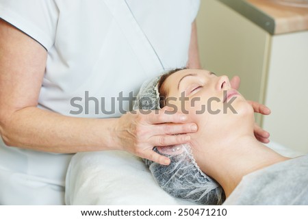 beautician worker with paintbrush applying facial cosmetic mask to female client in beauty salon
