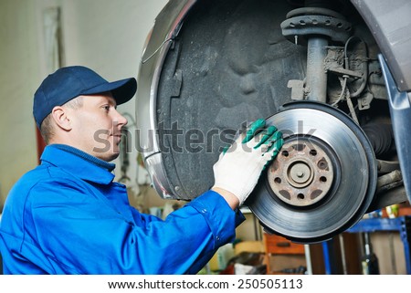 car mechanic worker repairing suspension of lifted automobile at auto repair garage shop station