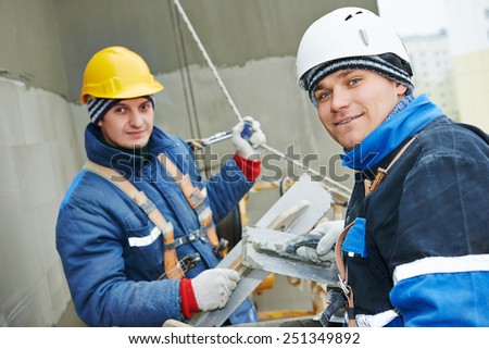 builders at facade plastering work during industrial building with putty knife float