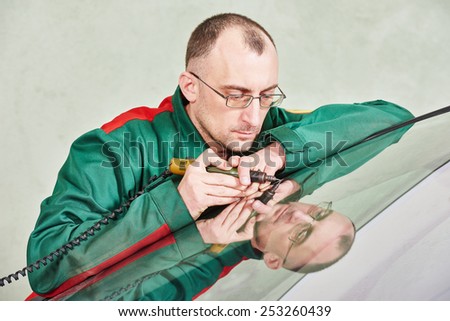 Automobile glazier repairman at windscreen repair of a car in auto service station garage
