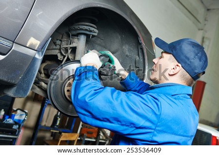 car mechanic worker repairing brakes of lifted automobile at auto repair garage shop station