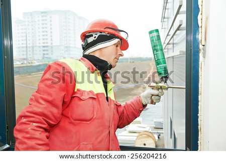 construction builder works with polyurethane foam during frame insulation at window installation