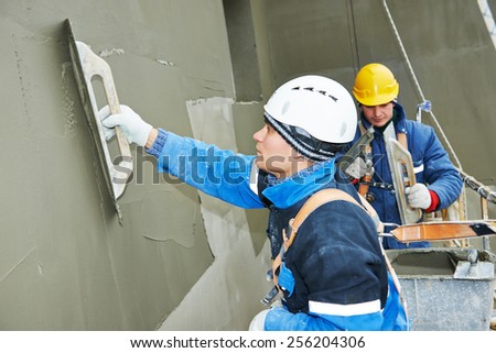 builders at facade plastering work during industrial building with putty knife float