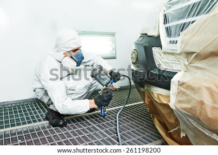 automobile repairman painter painting car body bumper in chamber
