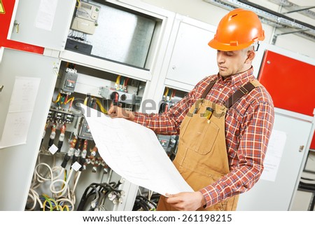 adult electrician builder engineer worker with electric scheme plan in front of fuse switch board