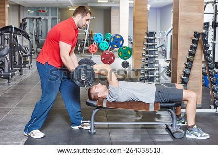 fitness and sport concept. personal coach trainer helps man work out at a gym with heavy weight