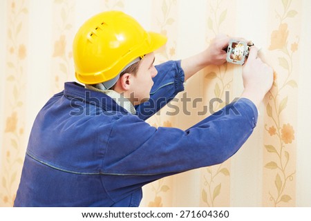 electrician worker at electric wall outlet or light switch socket installation work