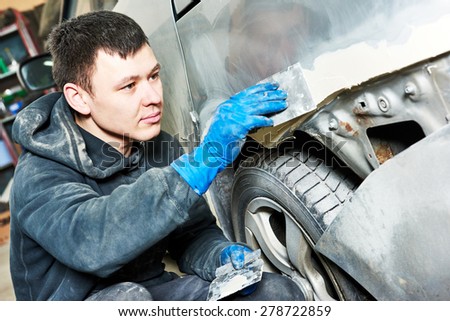 auto mechanic worker plastering body car at automobile repair and renew service station shop before painting restoration