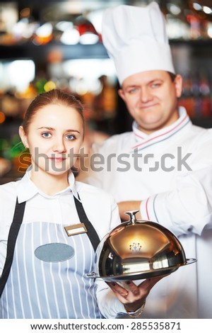 Waitress with tray cloche and cook chef at the indoor restaurant service