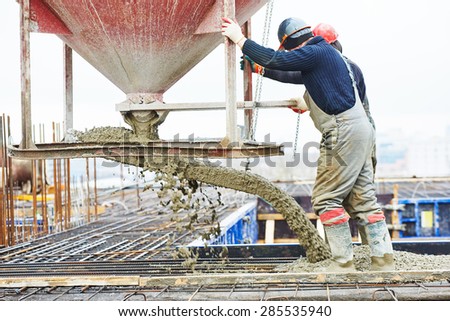 concreting work: construction site worker during concrete pouring into formwork at building area with skip