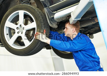 car mechanic inspecting suspension or brakes in car wheel of lifted automobile at repair service station
