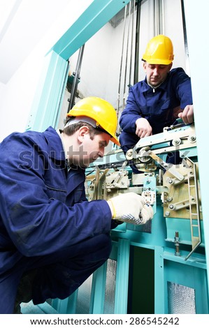 two male technician machinist worker at work adjusting elevator mechanism of lift with spanner