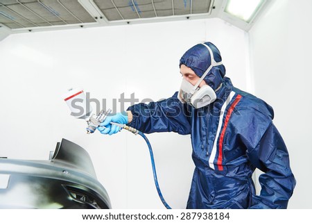 worker  painting auto car bumper in a paint chamber during repair work