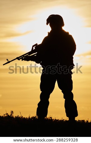 military. soldier silhouette in uniform with machine gun or assault rifle at summer evening sunset