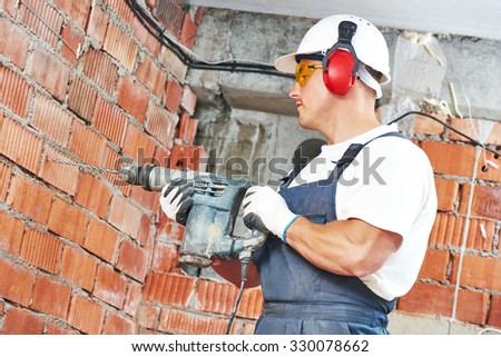 Builder worker with pneumatic hammer drill perforator equipment making hole in wall at construction site