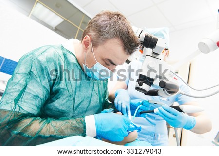 Dentistry. Dentist male doctor and assistant nurse working with microscope at dentistry office