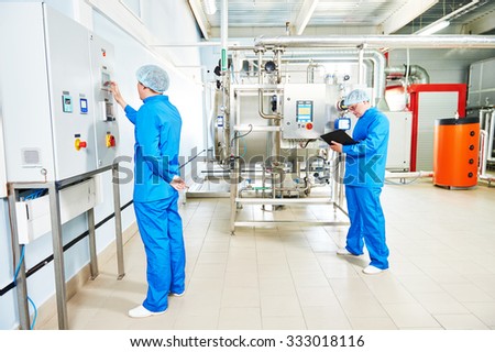 Two pharmaceutical male workers operating water preparation production line at pharmacy industry manufacture factory using notebook computer