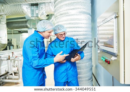 Two pharmaceutical technician male workers in air conditioning production line hall at pharmacy industry manufacture factory using notebook computer