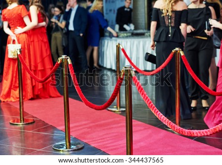 event party. red carpet entrance with golden stanchions and ropes. guests in the background