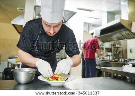 male cook chef decorating garnishing prepared salad dish on the plate in restaurant commercial kitchen